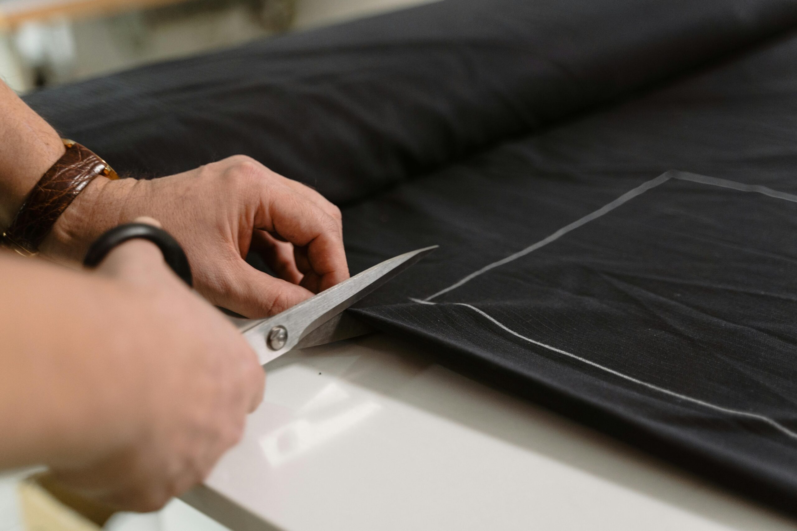 Close-up of a tailor's hand cutting black fabric with scissors, highlighting craftsmanship.